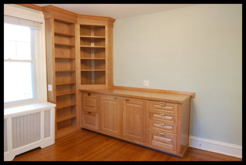Cherry wood attorney office cabinetry with 45 degree corner bookcase, raised panel doors, and custom file drawers.