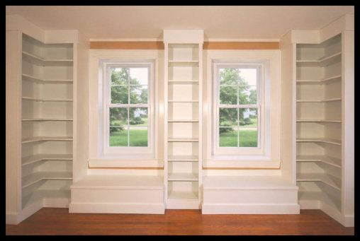Custom white built-in library with L-shaped flanking bookcases, window seats, and matching shelving between windows.