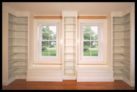 Custom white built-in library with L-shaped flanking bookcases, window seats, and matching shelving between windows.