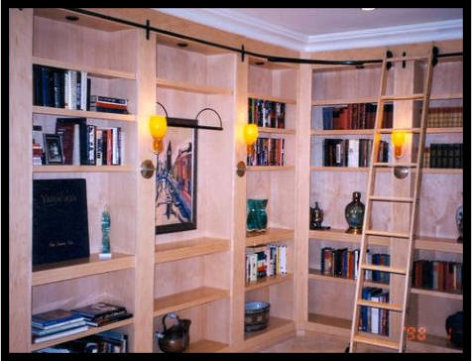 Custom 16-foot L-shaped maple library bookcase with rolling library ladder and sconce lighting. Premium craftsmanship, no particle board.