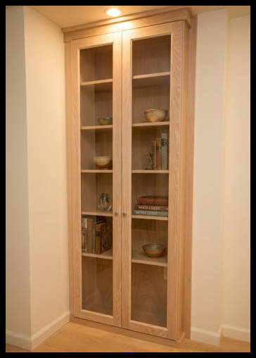 Oak wood built-in cabinet with double oak wood-framed glass doors.